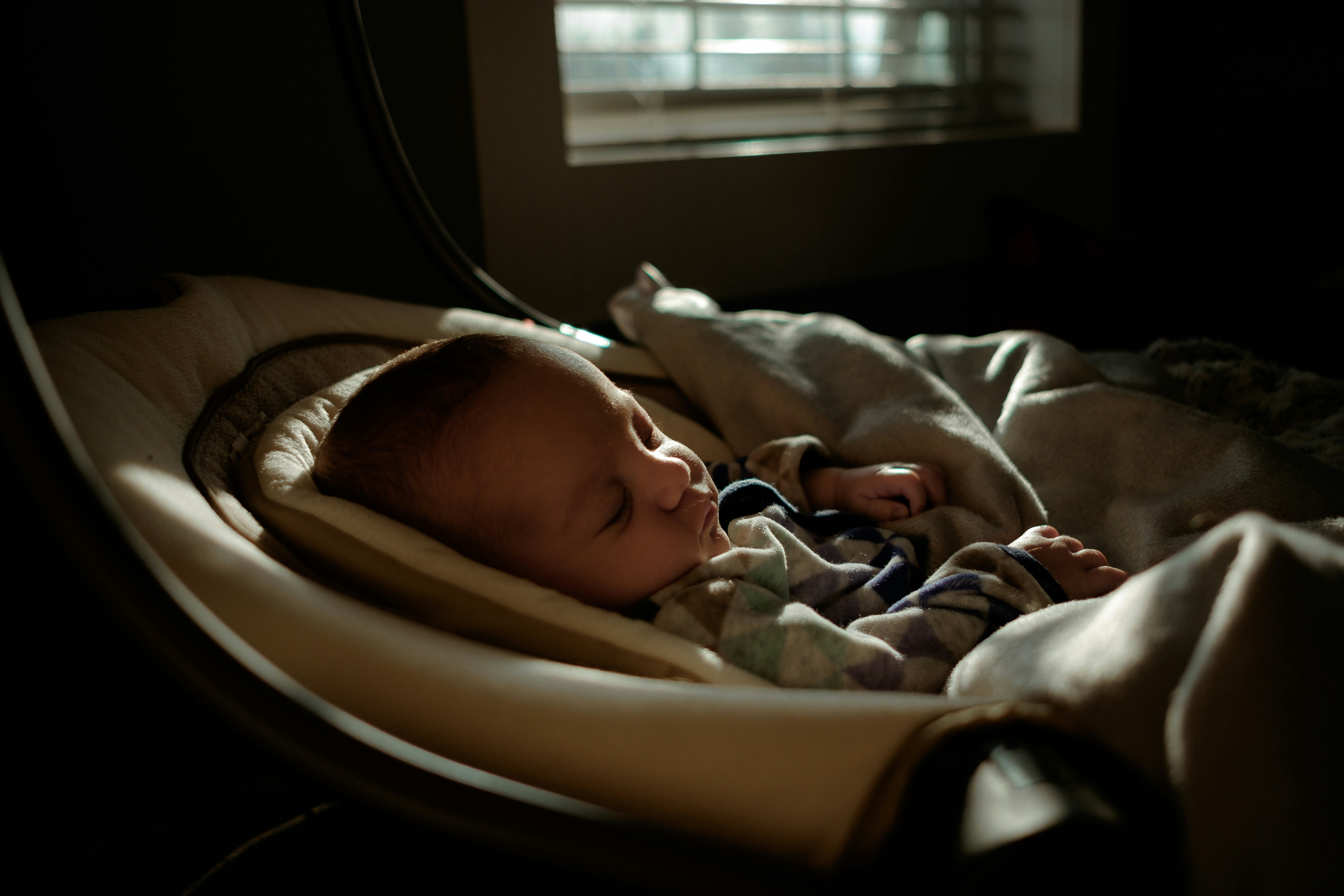 Newborn sleeping in soft natural window light, illustrating the innate biological drive to sleep governed by adenosine buildup and the circadian rhythm