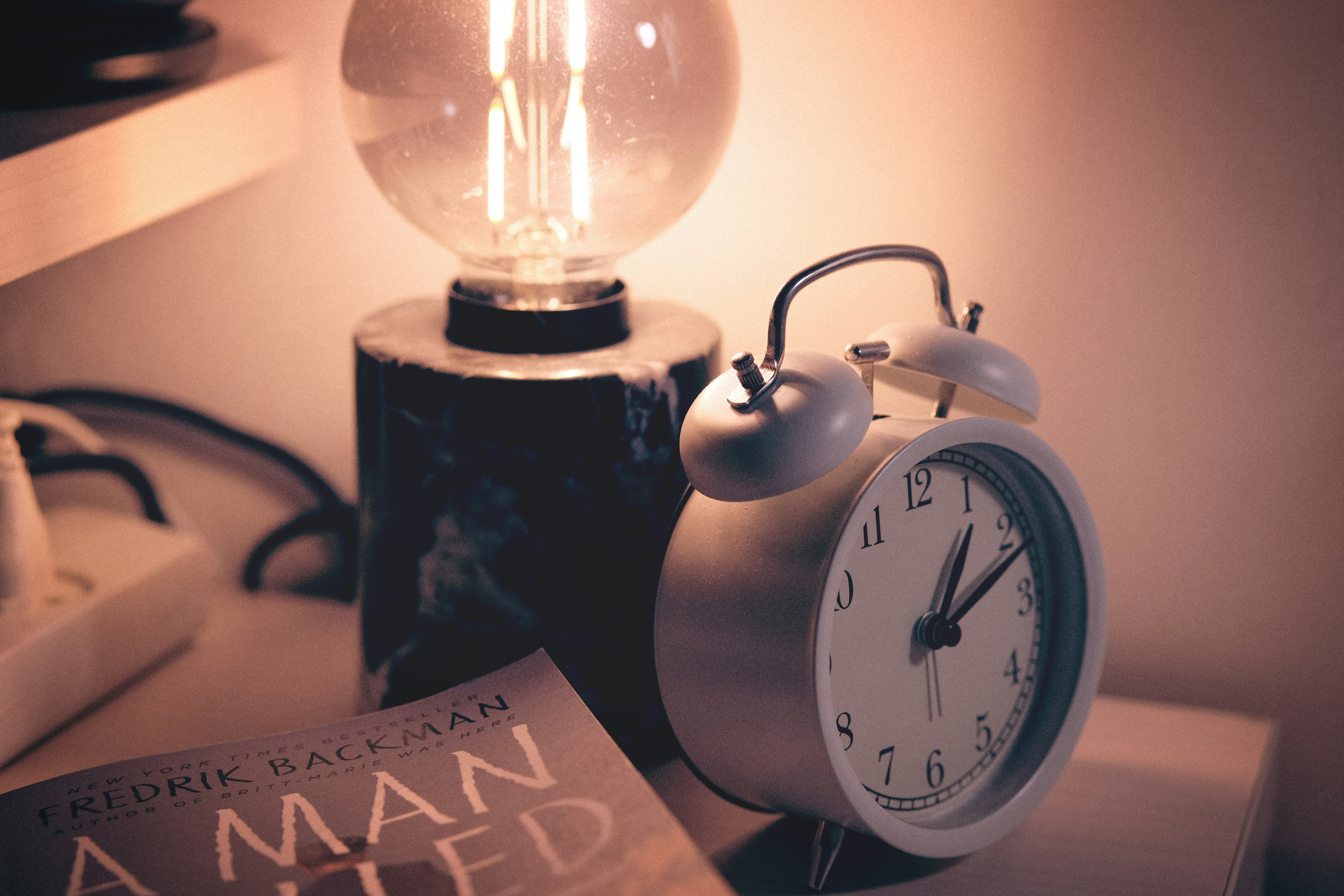 Alarm clock and warm bedside lamp on a nightstand, representing sleep timing and the nightly habit of monitoring sleep